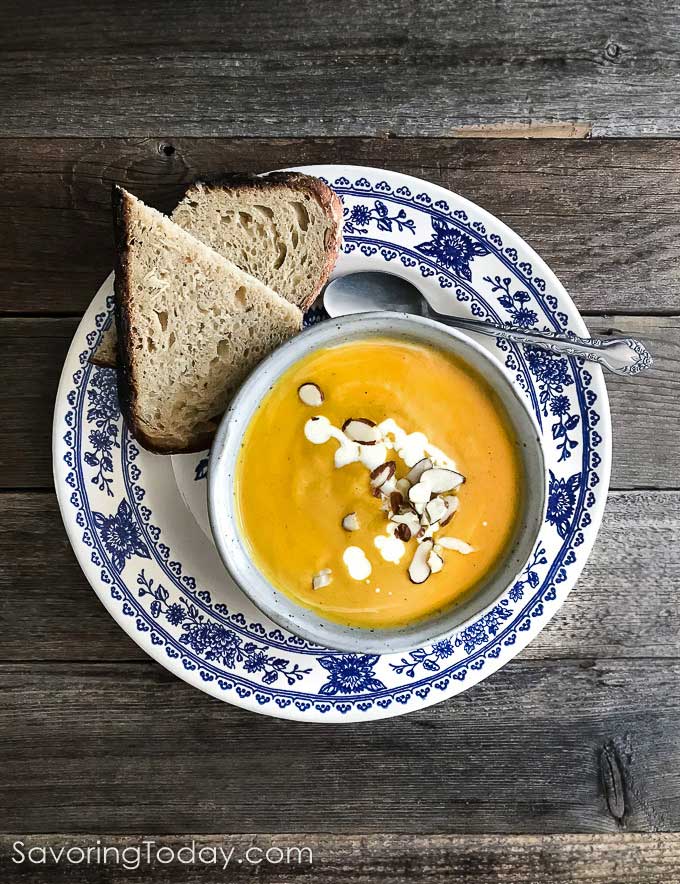 A warming bowl of butternut squash bisque is a fall favorite. Roasting the squash for this recipe is a must as it deepens the flavor of every bite. Butternut soup in a bowl on a blue and white plate with dipping bread.